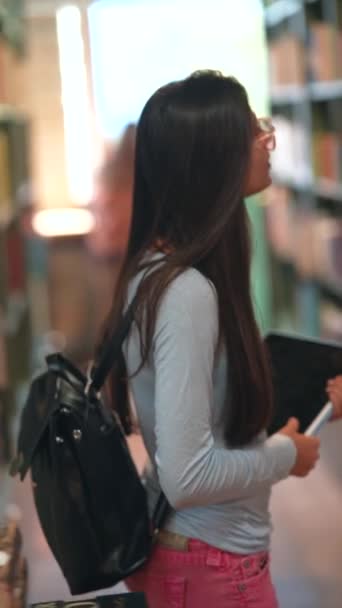 Яскрава молода жінка ходить серед книжкових полиць у книгарні. Високоякісні 4k кадри - Кадри, відео
