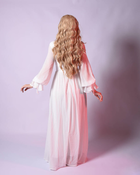 Full length portret van blonde vrouw dragen witte historische bruids jurk fantasie kostuum jurk. Staande houding, naar achteren kijkend, weg lopend van de camera. geïsoleerd op studio achtergrond. - Foto, afbeelding