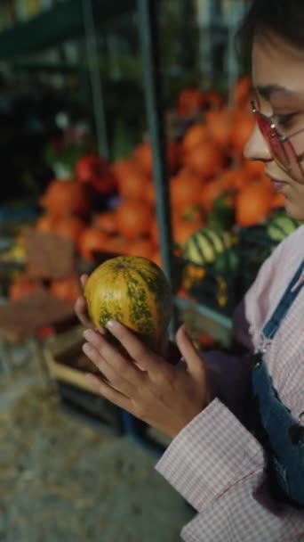 Uma agricultora é vista entusiasticamente mostrando a abóbora de listras verdes à venda no mercado. Imagens 4k de alta qualidade - Filmagem, Vídeo