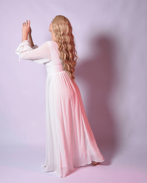Retrato de cuerpo entero de mujer rubia vestida con vestido de novia histórico blanco vestido de fantasía. Posar de pie, mirando hacia atrás alejándose de la cámara. aislado en el fondo del estudio. - Foto, imagen