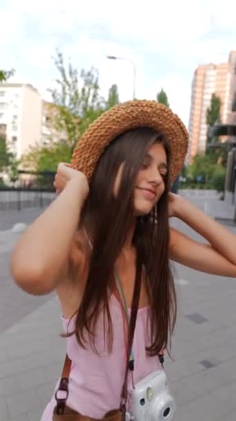 Грациозная юная леди в шляпе, вооруженная камерой, идет по улицам города. Высококачественные 4k кадры - Кадры, видео