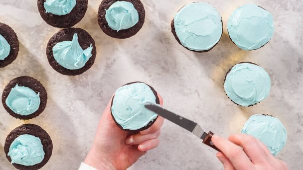 Flat lay. Step by step. Scooping blue buttercream frosting on top of the chocolate cupcakes. - Photo, Image