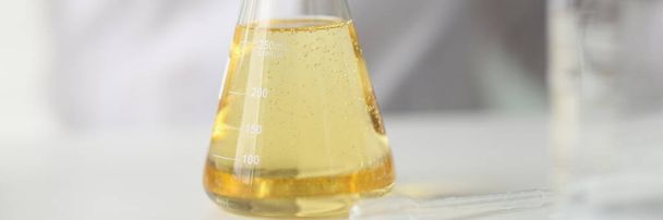Zbliżenie kolby żółtym płynem na stole laboratorium badawczego. Koncepcja eksperymentów chemicznych i naukowych. - Zdjęcie, obraz