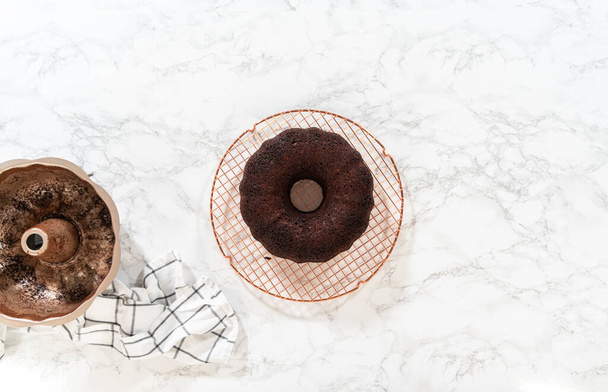 Flat lay. With precision, the Chocolate Bundt Cake is carefully removed from the pan - placed onto a round cooling rack, preparing it for a flawless presentation and delightful indulgence. - Photo, Image