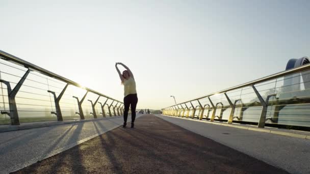 Un nouveau jour, une nouvelle course : une femme s'engage dans un rituel de réchauffement matinal avant le jogging urbain au lever du soleil. Images 4k de haute qualité - Séquence, vidéo