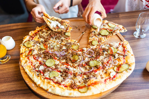 食べ物,人,食べるコンセプト.木のテーブルにスライスした自家製のピザを共有する手の閉鎖.ピザ屋でピザを取る若者. - 写真・画像
