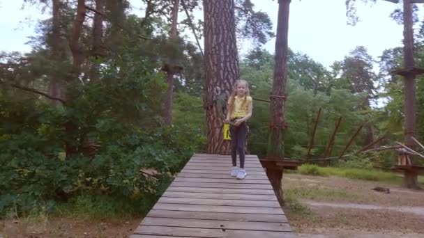 Ein Kind in einem Wald-Erlebnispark aus Seilen. Das Mädchen klettert mit einem Hochseil den Pfad hinauf. Outdoor-Kletterzentrum für Kinder. Spielplatz für Kinder und Sport mit der Seilbahn. - Filmmaterial, Video
