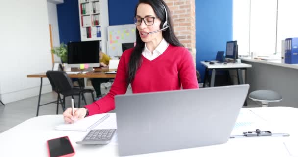 Mujer con auriculares con micrófono trabajando detrás de la película portátil 4k. Trabajo en concepto de centro de llamadas - Metraje, vídeo