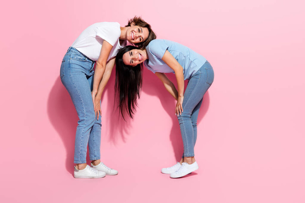 Full body cadre of two toothy smiling girls jeans stylish t shirt flexibility friends have fun bent isolated on pink color background. - Фото, изображение