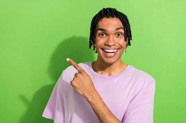 Portrait of funny amazed youngster guy wearing hair cornrows directing finger empty space news isolated green color background. - Foto, afbeelding