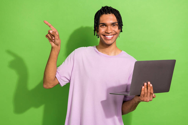 Photo of handsome cheerful man toothy smile hold netbook indicate finger empty space isolated on green color background. - Fotoğraf, Görsel