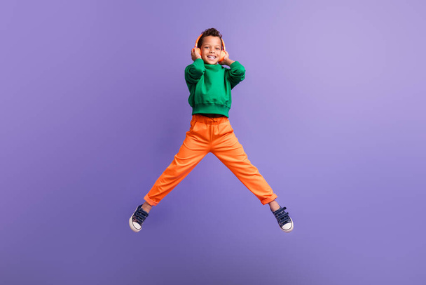 Photo of cheerful nice boy wear stylish green outfit listen mp3 player wireless device isolated on purple color background. - Fotó, kép