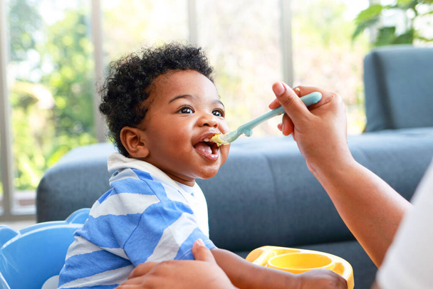 Happy smiling boy with mom while eating in the living room at home. Preschool child development, food menu for 1 year olds - Photo, Image