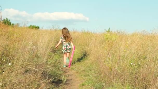 Une petite fille court à travers un champ d'été avec un cerceau de gymnastique à la main. - Séquence, vidéo