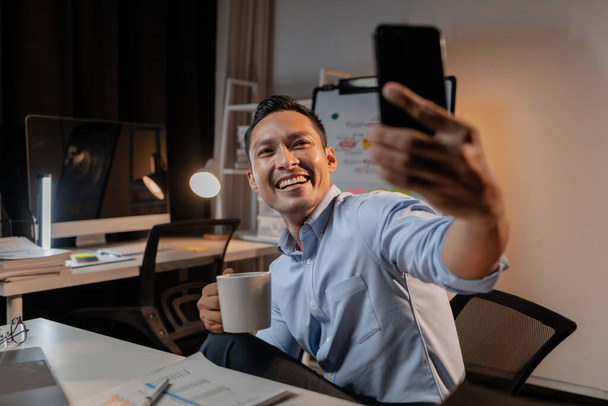 Азиатский бизнесмен пользуется мобильным телефоном в офисе, он молодой и энергичный руководитель компании, управляющий компанией, чтобы расти и усердно работать для получения прибыли. Концепции управления стартапом. - Фото, изображение