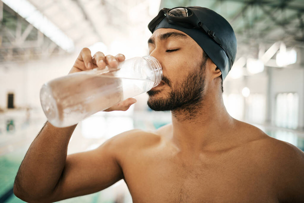 Άνθρωπος, κολυμβητής και πόσιμο νερό για ενυδάτωση, άσκηση ή προπόνηση στην εσωτερική πισίνα. Ενεργός και διψασμένος άνδρας ή αθλητής με μεταλλικό ποτό για βιωσιμότητα, φυσική κατάσταση ή καρδιο. - Φωτογραφία, εικόνα