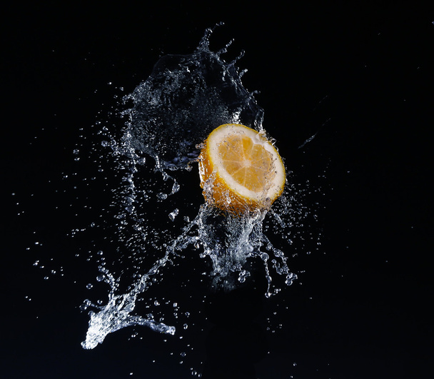 Un chupito de limón a alta velocidad con agua salpicada, sobre un fondo negro
. - Foto, Imagen
