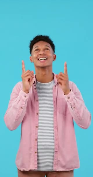 Happy, face and man pointing up in studio for news, announcement or notification on blue background. Excited, smile and guy model with hand sign show space, service or opportunity, sign up or offer. - Footage, Video