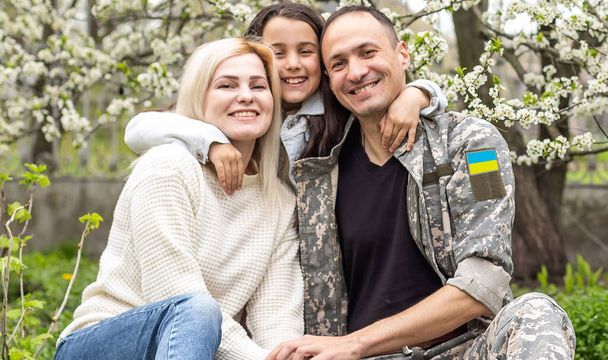 Στρατιώτης με στρατιωτική στολή επανενώθηκε με την οικογένειά του και την ουκρανική σημαία. - Φωτογραφία, εικόνα