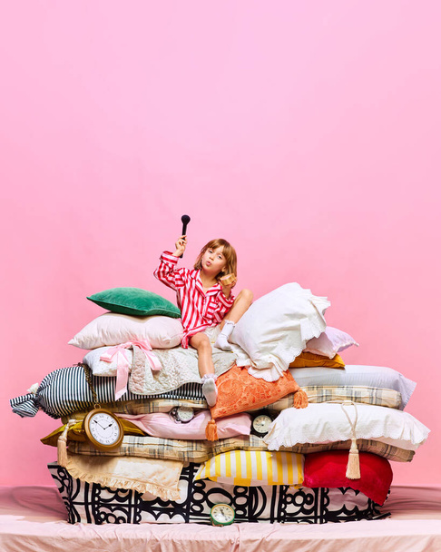Ritratto di bella principessina fare make up su grande letto di piume con cuscini su sfondo rosa studio.Concetto di bellezza, moda, fantasia, storico, fata remake, vendita, stile, cosmetici. Pubblicità - Foto, immagini