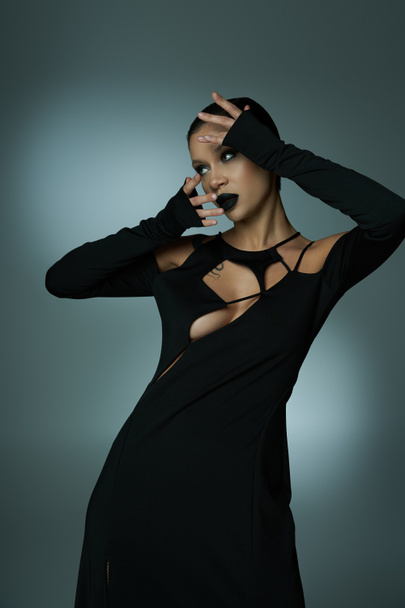 Диявольська краса, стильна жінка в моторошному макіяжі та чорному костюмі на Хеллоуїн дивиться на сірий - Фото, зображення
