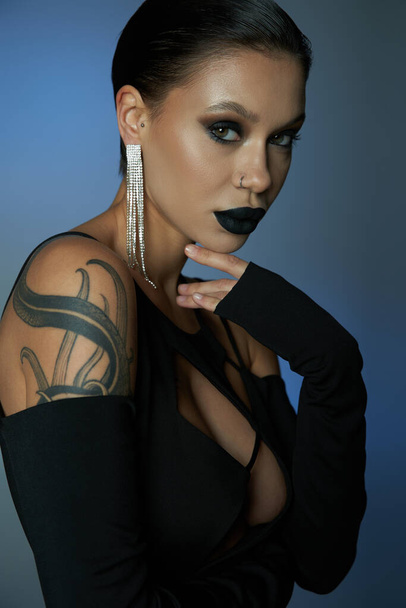 mujer tatuada con maquillaje misterioso oscuro mirando a la cámara en el fondo azul y gris, concepto de Halloween - Foto, Imagen