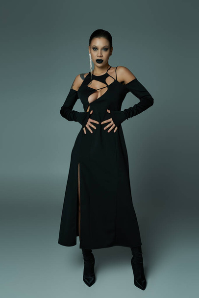 longitud completa de la mujer hechizante en el vestido de la hechicera negro y maquillaje en gris, concepto de Halloween - Foto, Imagen