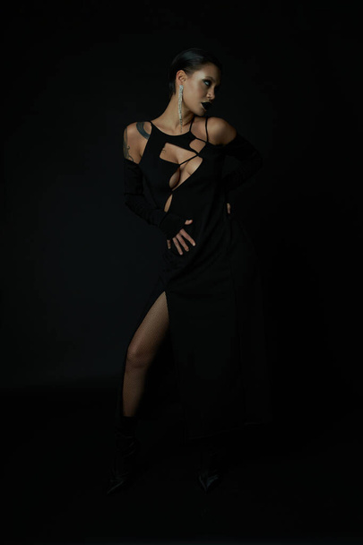 magic sensuality, tattooed woman in black sexy dress posing in darkness in studio, halloween concept - Zdjęcie, obraz