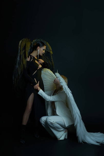 Niebiański anioł trzymając za rękę ciemnego demona stojącego na czarnym tle, kobiety w kostiumach na Halloween - Zdjęcie, obraz