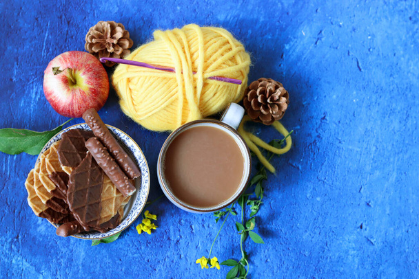 Xícara de café com leite, waffles, maçãs e bolas de chocolate e fios em um fundo azul com espaço de cópia. Conceito de outono acolhedor.  - Foto, Imagem