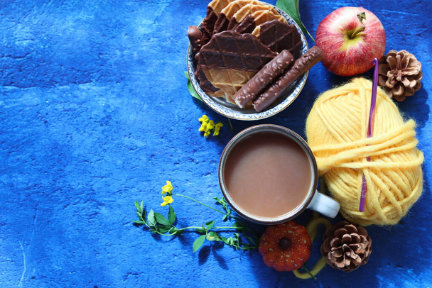 Taza de café con leche, gofres, manzanas y bolas de chocolate e hilo sobre un fondo azul con espacio para copiar. Acogedor concepto de otoño.  - Foto, imagen