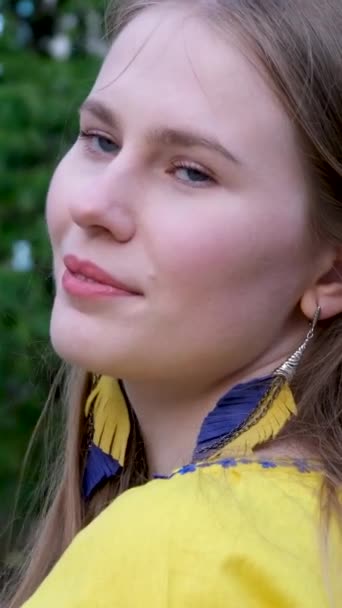 mladá krásná žena, mladá dívka ve velkém městě ve žluté vyšívané košili, vyšívaná blůza, dlouhé hnědé vlasy, úsměv péřové náušnice, žluté a modré barvy v oblečení, ukrajinský národní kostým - Záběry, video