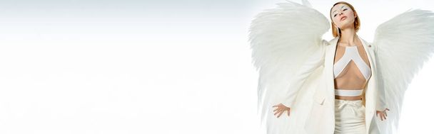 όμορφη αγγελική γυναίκα σε αποκριάτικο κοστούμι με ουράνια φτερά ποζάρουν σε λευκό, banner - Φωτογραφία, εικόνα