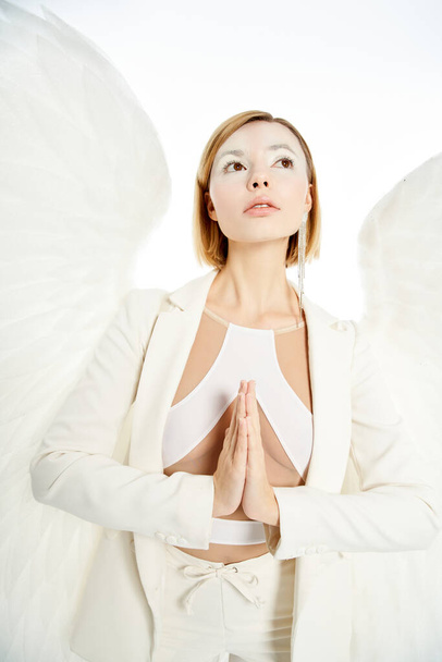 woman with angelic face and light wings looking away and praying on white backdrop - Photo, Image