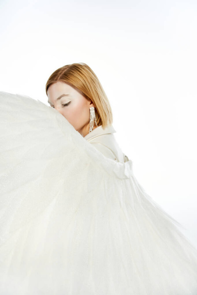 woman with angelic aura obscuring face with divine wings on white backdrop, purity and serene - Photo, Image