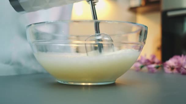 Kobieta bije białko jajka w głębokiej misce mikserem z dużą prędkością. Zbliżenie stołu. Gotowanie w kuchni - Materiał filmowy, wideo