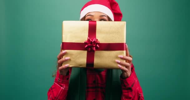 Junge Frau versteckt sich hinter Weihnachtsgeschenk, offenbarende Augen, Studiovideo. Hochwertiges 4k Filmmaterial - Filmmaterial, Video