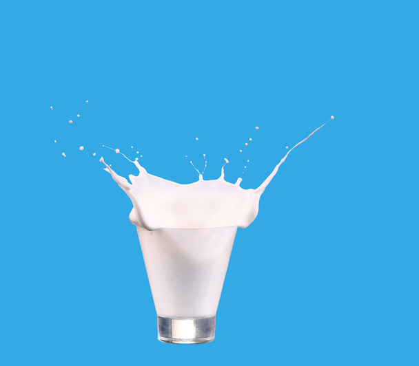 Milch in ein Glas gießen, isoliert vor blauem Hintergrund - Foto, Bild