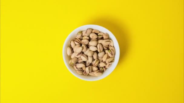 Pistachios in a bowl on a bright yellow background. Stop motion video with the pistachios nuts disappear from the white ceramic bowl. - Footage, Video
