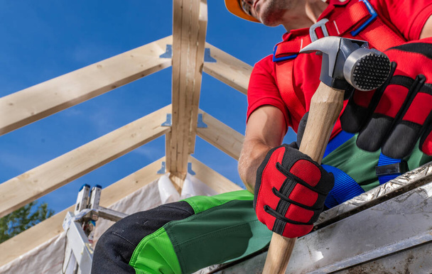 Bauunternehmer mit großem Hammer unter Holzskelettgerüst eines Gebäudes - Foto, Bild