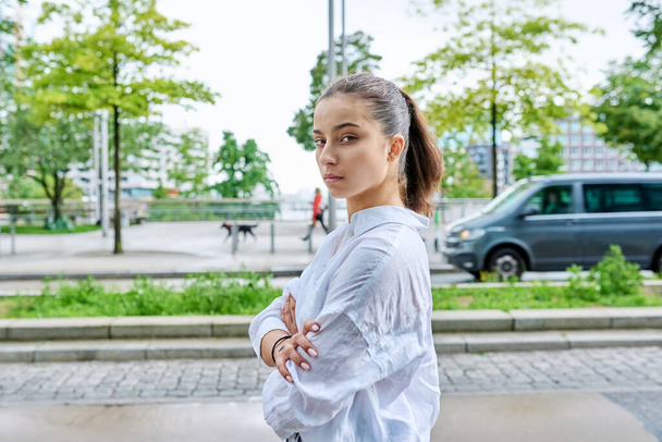 Portrait of serious confident teenage girl looking at camera, with crossed arms on street of modern city. Adolescence, urban lifestyle, young people concept - Foto, Imagen
