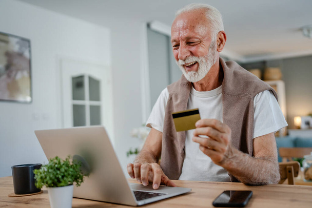 Un hombre mayor caucásico abuelo masculino sentarse en casa uso de la tarjeta de crédito y ordenador portátil de compras en línea uso de Internet para la compra en línea activa moderna senior - Foto, Imagen