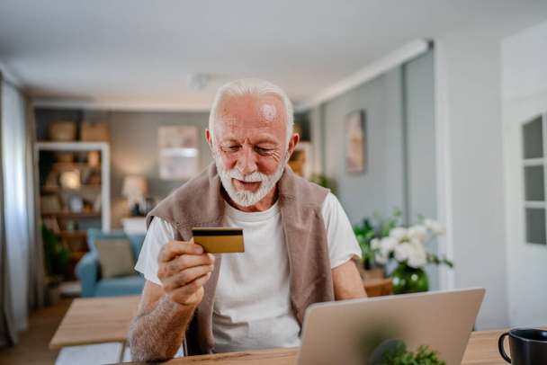 Egy férfi vezető kaukázusi férfi nagyapa otthon ülni használja hitelkártya és laptop számítógép vásárlás online internet online vásárlás aktív modern senior - Fotó, kép