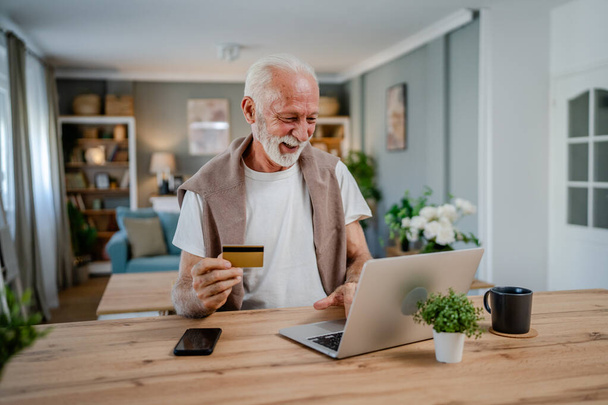 Un hombre mayor caucásico abuelo masculino sentarse en casa uso de la tarjeta de crédito y ordenador portátil de compras en línea uso de Internet para la compra en línea activa moderna senior - Foto, imagen