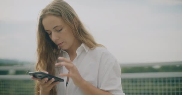 スマートフォンでサーフィンする魅力的なブロンドの若い女性のスローモーションショット - 映像、動画