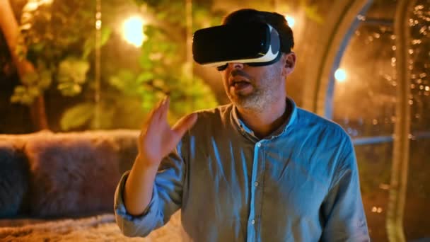 Mluvící muž ve VR brýlích sedí uvnitř glamping stanu s osvětlením v noci - Záběry, video