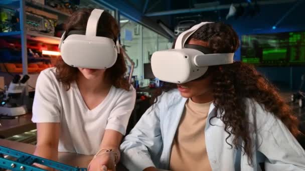Две молодые женщины в очках виртуальной реальности проводят эксперименты по робототехнике в лаборатории. Робот на столе - Кадры, видео