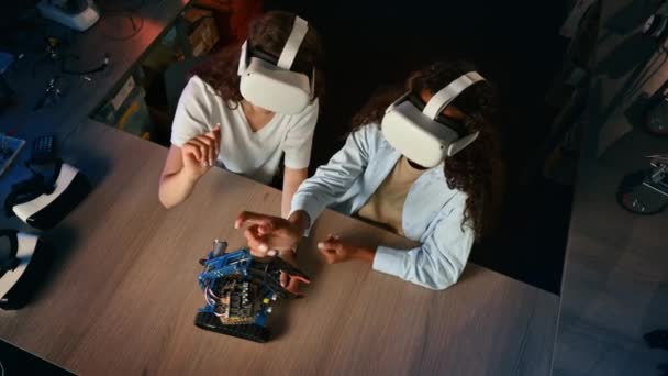 VR gözlüklü iki genç kadın bir laboratuvarda robotik deneyler yapıyor. El kol hareketi. Robot masada. - Video, Çekim