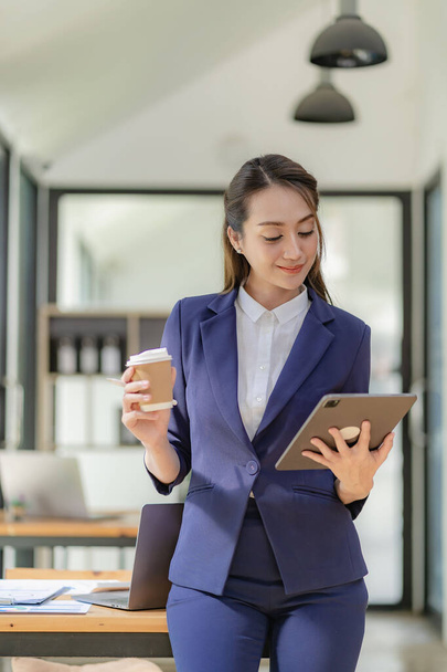 Asian businesswoman holding digital tablet and standing in front of his desk, creative concept Successful business woman in business - Foto, afbeelding