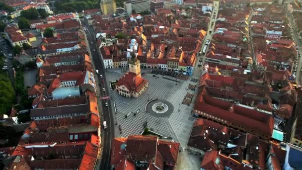 Vista aérea do drone da Praça do Conselho em Brasov ao nascer do sol, Roménia. Centro da cidade velha com County Museum of History, edifícios antigos ao redor, colinas com vegetação - Filmagem, Vídeo
